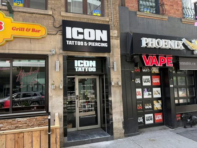 Illuminated black sign box for ICON TATTOO & PIERCING on a brick storefront