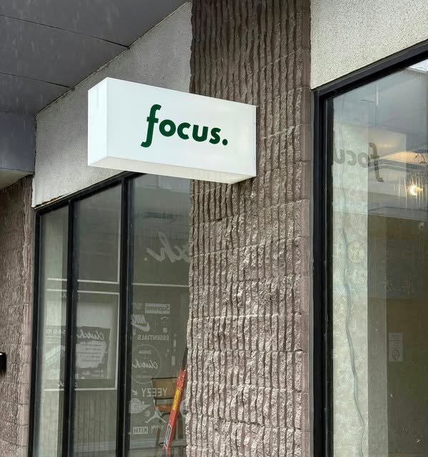 White illuminated acrylic projecting sign box reading 'focus.' on a concrete facade